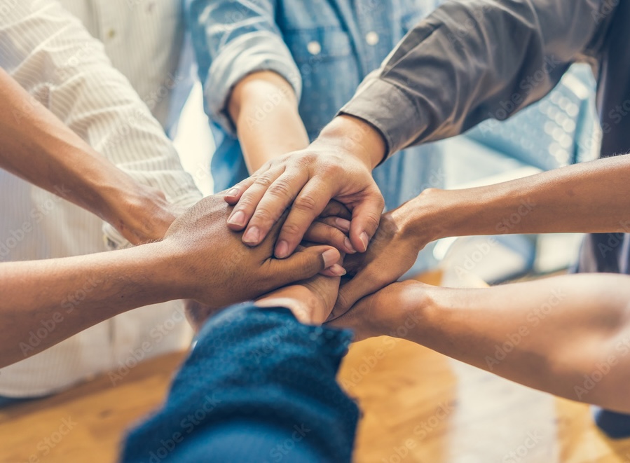 A close up image of eight arms in a circle with hands in the middle showing teamwork.