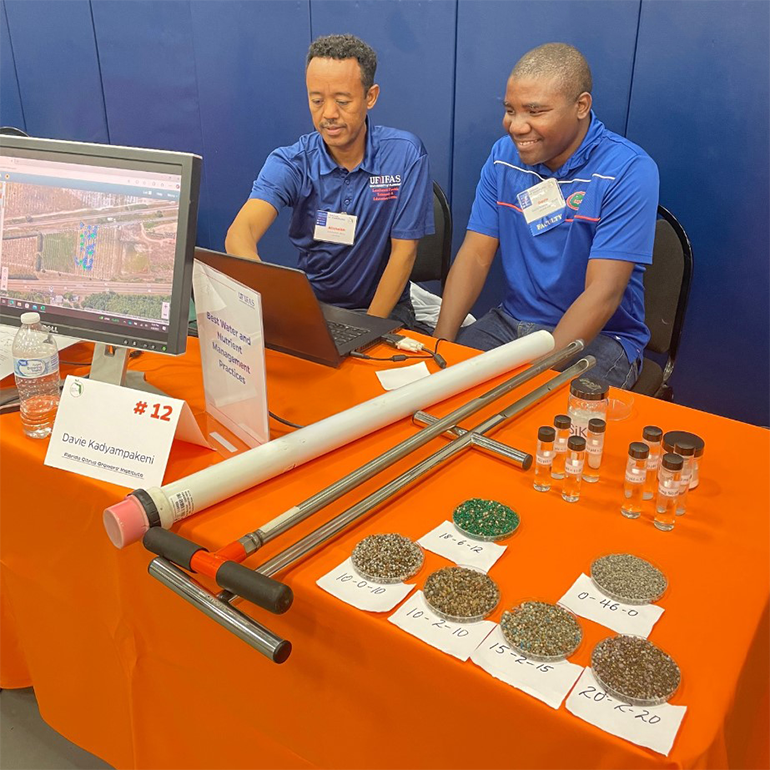 Two scientists sit behind a table, looking at a laptop computer. The table is covered with best management practices tools for citrus growers.