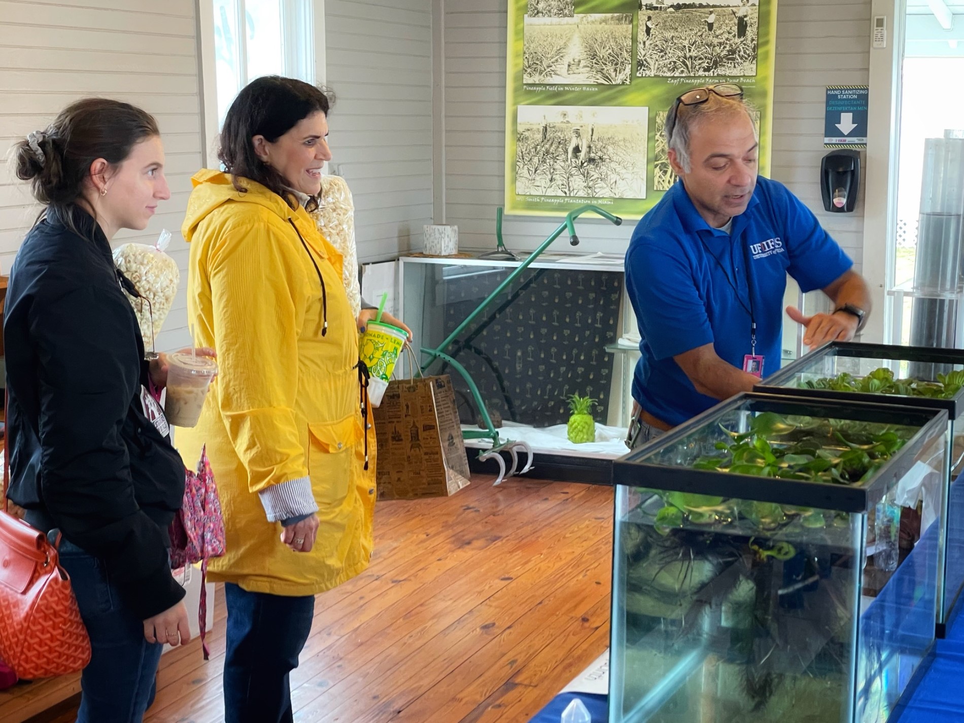 A professor standing by two aquariums with aquatic plants growing, explains water quality to two women attending the South Florida Fair.