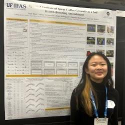 A female college student stands in front of her research poster hanging on a bulletin board.