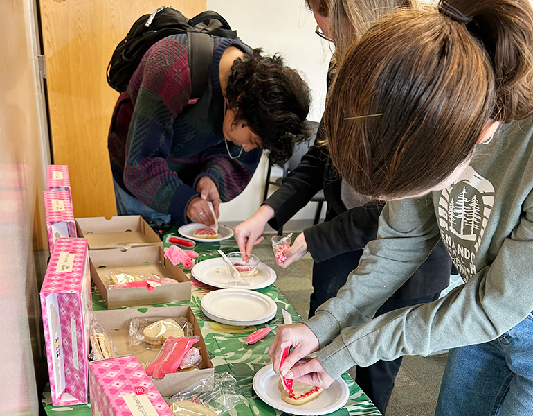 Three people bent over a cabinet, decorating Valentine's Day cookies.