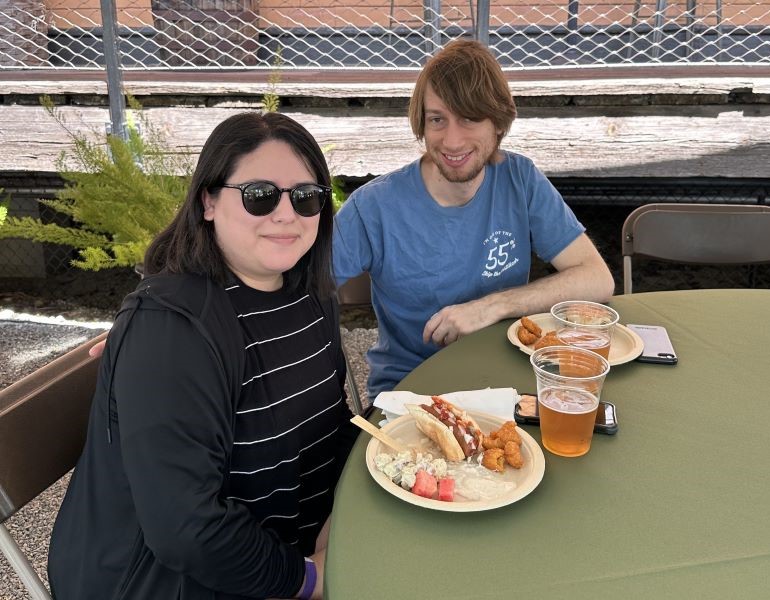 A woman and a man sitting at a table under a large tent, eating a picnic lunch.