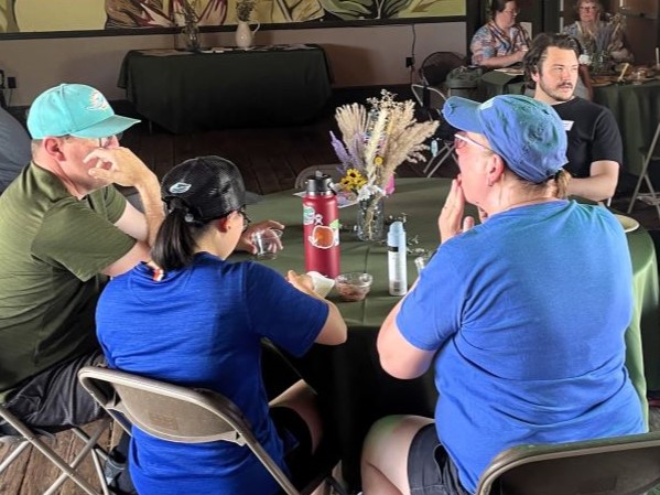 Four people sitting at a table in an old train depot, eating a picnic lunch.