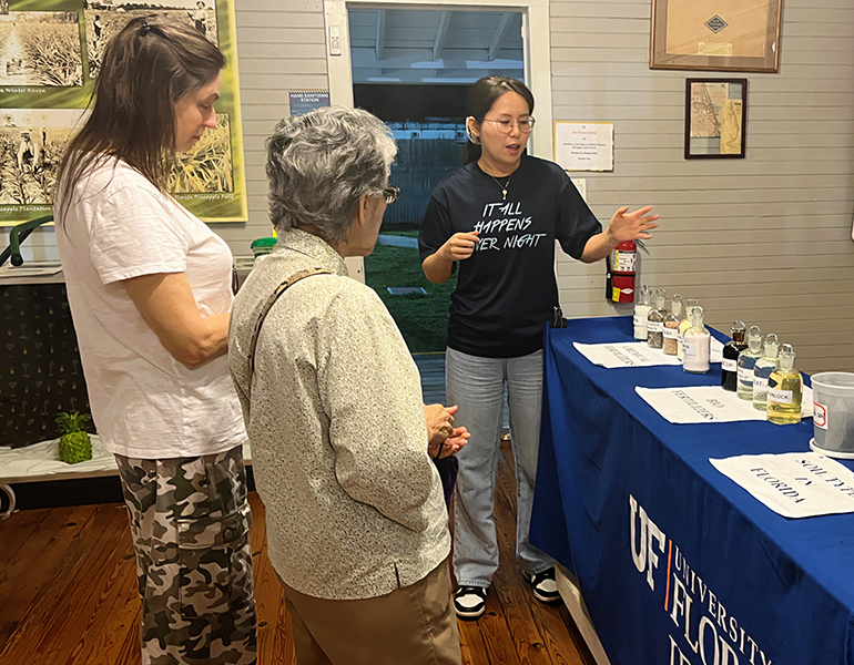 Two women stand at a table with various samples of soil while a female graduate student explains the display.