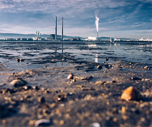 Soil, Water, Public Health course image showing a shallow pond in the foreground with industrial smokestacks in the distance