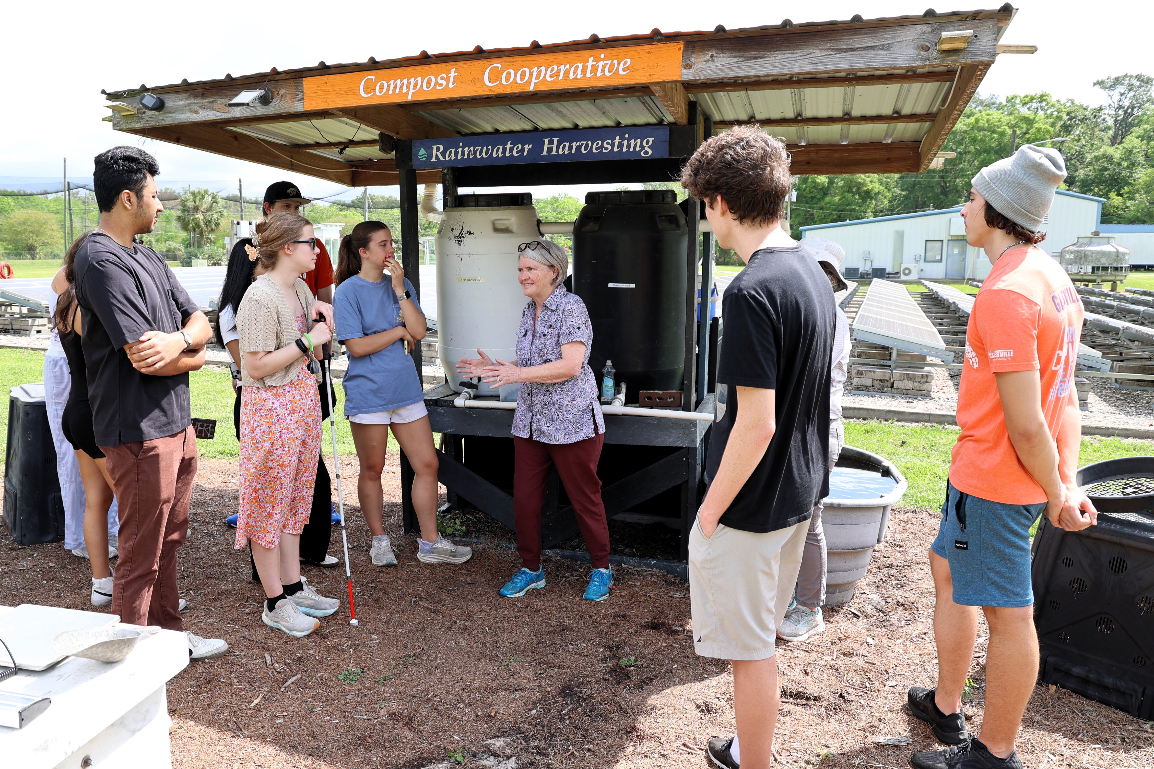 A group of students stand around a professor who is explaining a rainwater harvesting system.