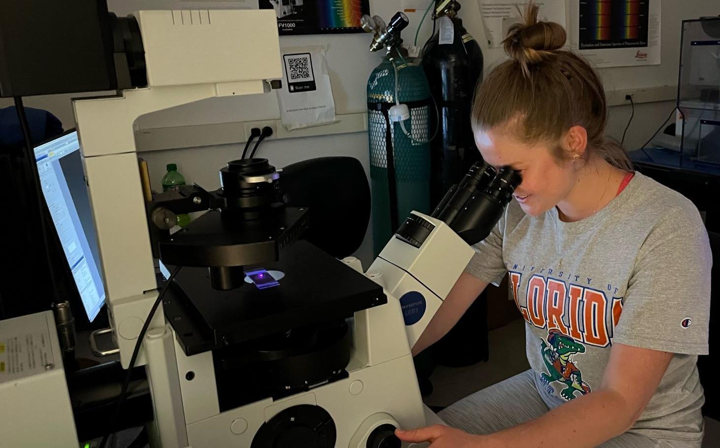A college student in a lab looking through a microscope at drinking water treatment residuals, in search of microplastics.