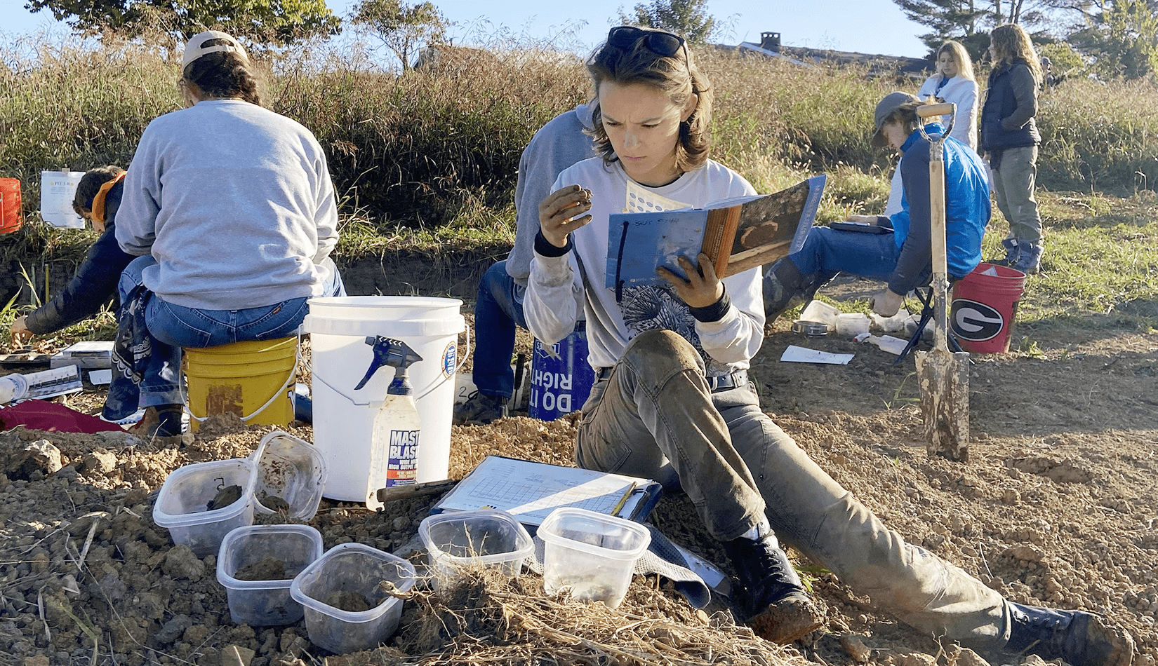 Katya Kasprzak sits on the ground, analyzing a soil sample for texture and color at a soil judging competition.