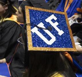 An image of graduates at a commencement ceremony with one person's mortarboard emblazoned with the letters U F with blue and orange glitter material.